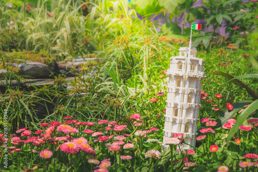 Obraz premium LEGO Architecture Leaning Tower of Pisa model displayed among blooming pink daisies in a sunny garden bed for commercial stock photography