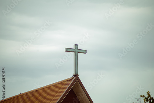 Christian Cross Rising Above a Church Roof Against a Dramatic Cloudy Sky