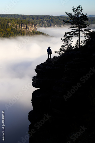 Фотография The silhouette of a lonely man stands on the edge of a rock above the Elbe river