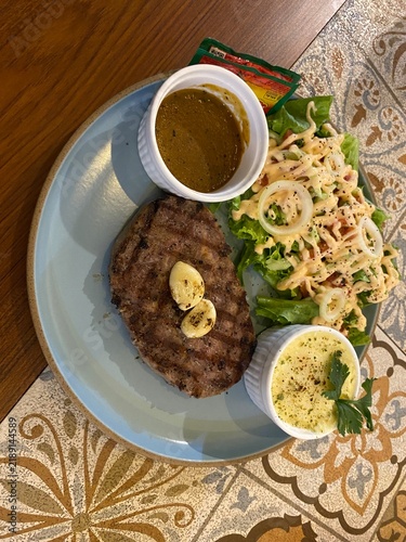 Canvastavla Grilled beef steak topped with garlic butter served with fresh salad, creamy side, and gravy sauce on a blue plate over a patterned table