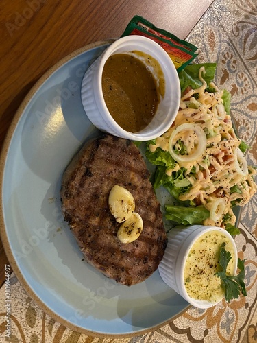 Foto Grilled beef steak topped with garlic butter served with fresh salad, creamy side, and gravy sauce on a blue plate over a patterned table