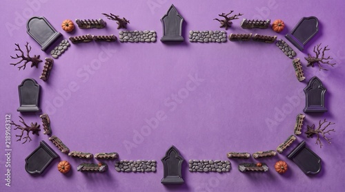 A festive halloween frame made of miniature black tombstones and spooky trees arranged on a vibrant purple background surface