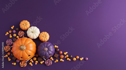 Top view of assorted decorative pumpkins and autumn gourds arranged on a solid dark purple background with copy space