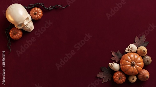 Halloween background featuring a human skull and small decorative pumpkins arranged on a deep dark red velvet fabric surface
