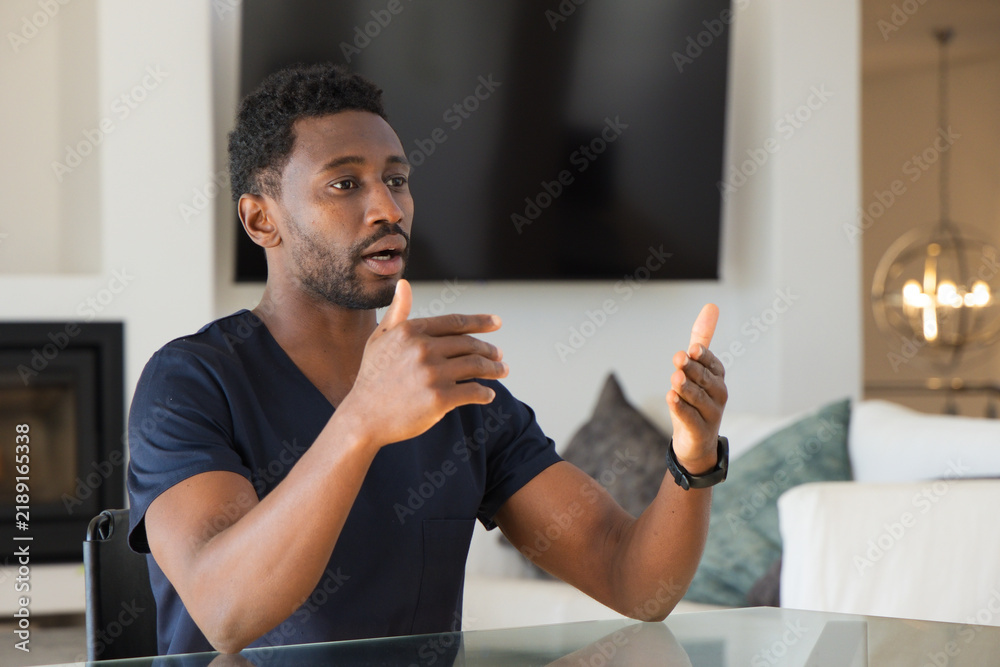 Obraz premium African American man wearing navy scrubs and watch, talking and gesturing at glass table at home