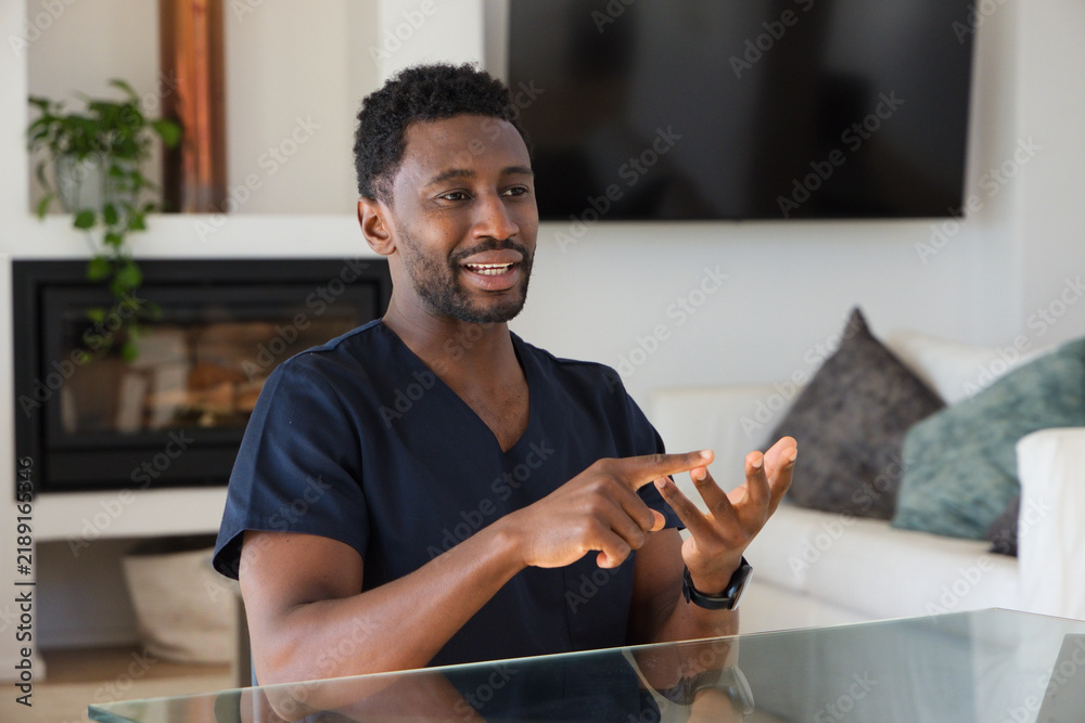 Naklejka premium Man in navy scrubs and wristwatch sitting at glass table in living room near TV gesturing
