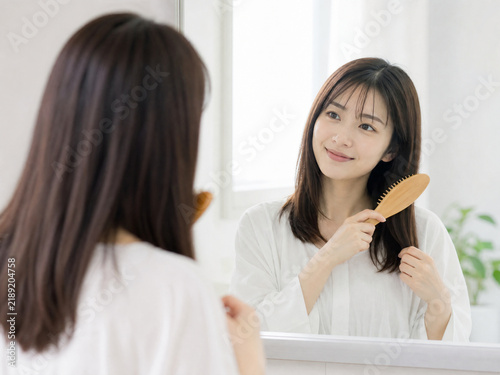 洗面所の鏡の前で木のヘアブラシを使って髪をとかす女性