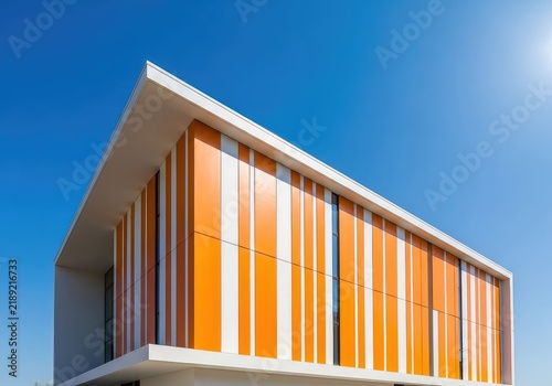 A modern architectural structure stands tall under a bright blue sky, featuring bold orange stripes on its side facade for a vibrant look, outdoor, aesthetic, office