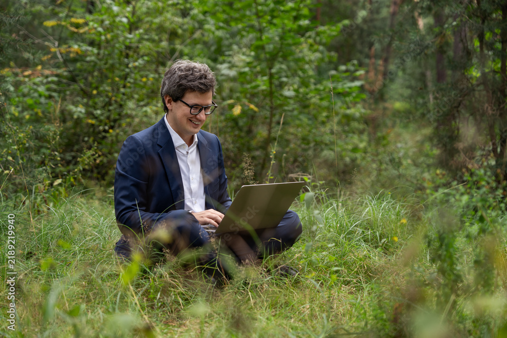 Obraz premium Smiling man working on laptop in green forest, blending freelanc