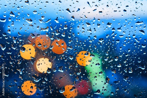 Water raindrops on glass window with blurred city street bokeh lights background