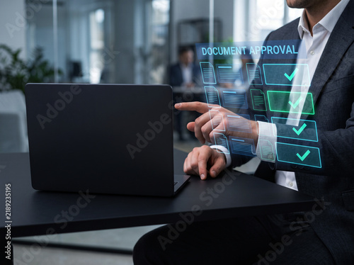 Corporate worker pointing at document approval holographic interface while managing project workflow at desk in busy modern office meeting environment.