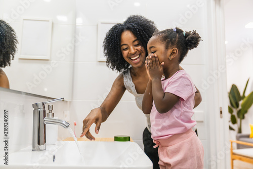 Fotografía Happy african american mother and daughter washing face in bathroom, teaching hy