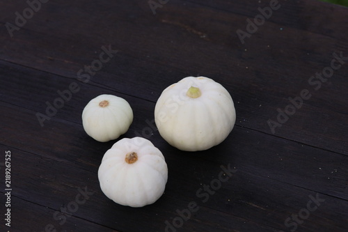 Three small white decorative pumpkins on a dark rustic wooden background