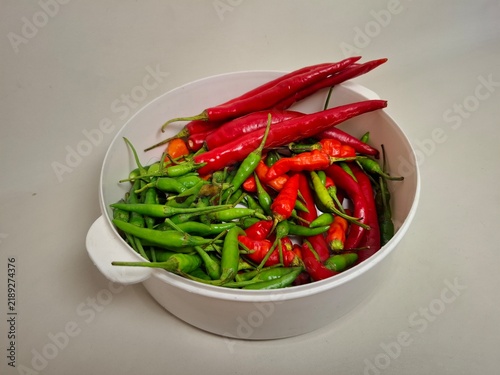 фотографія Fresh red, green, and orange chili peppers arranged in a white colander against a neutral background