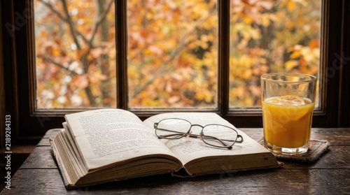 Cozy autumn scene with open book and orange juice by a window