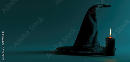 Black witch hat and candle on dark teal Halloween background