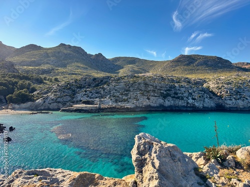 view over the bay Cala Barques and Cala Clara with turqouise water near Cala Sant Vicenc in northeastern Mallorca, rocky cliff and the Serra de Tramuntana mountains behind, Spain