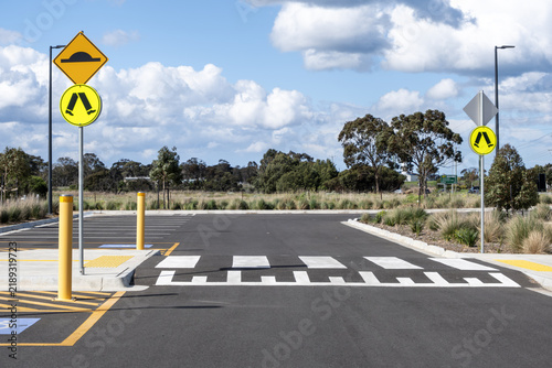 A raised pedestrian zebra crossing within a public car park facility, featuring road signage for speed humps and pedestrian safety, bollards, tactile paving, and clear road markings in Australia