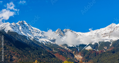 The landscape view of Snow-Capped Mountain Peaks  and forest autumn trees scene background under a Clear Blue Sky