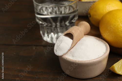 Foto Baking soda in bowl, scoop, lemons and water on wooden table, closeup