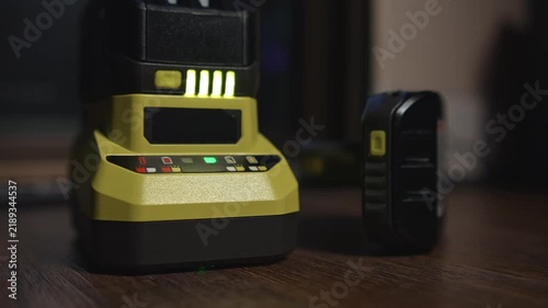 Power tool battery on charger with illuminated level indicator lights demonstrating charging process and current battery status on floor