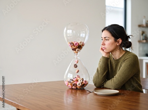 Woman watching donut sand falling through giant hourglass on table