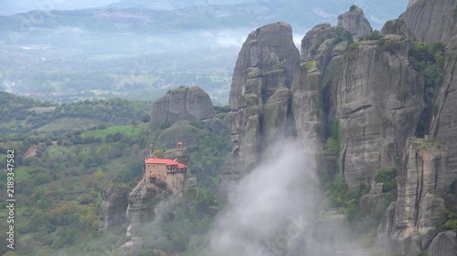 Stunning monastery perched atop massive rock formations in meteora greece during misty morning.
