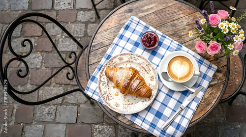 A beautifully plated croissant and cafe from France, featuring a golden, flaky croissant next to a steaming cup of coffee, with a Parisian cafe table setting, complete with a checkered napkin .