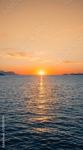 Golden sunset over the calm ocean horizon with soft light reflecting on the water surface