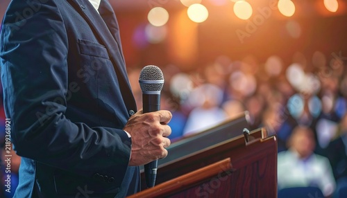 Speaker holding microphone at conference podium  public speaking and professional presentation