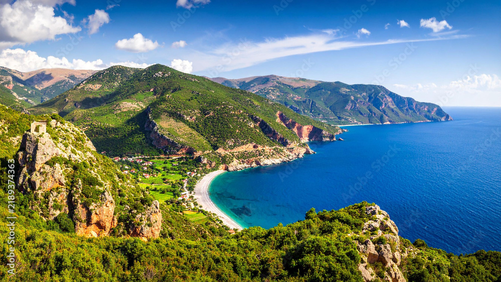 Obraz premium Scenic coastal landscape with turquoise sea, green mountains, and blue sky on a sunny day