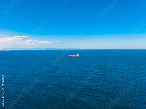Quadro su tela Cargo ship sailing on clear blue waters under a blue sky near the coast during d