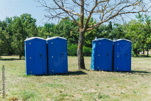 Bild auf Leinwand Group of blue portable toilets placed near a bare tree in an open field under cl