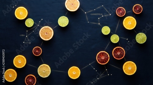 Sliced Citrus Fruits Flat Lay with Constellation Map on Dark Surface