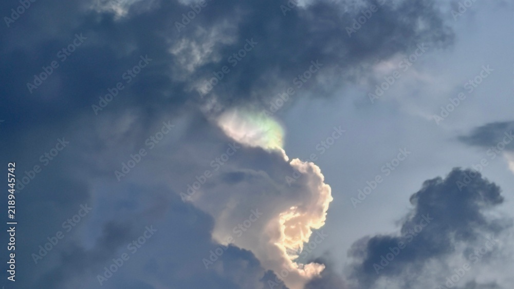 Obraz premium Iridescent cloud formation displaying soft rainbow colors against a backdrop of deep dark stormy skies