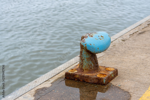 Obraz na płótnie Weathered blue bollard on a concrete pier by the water