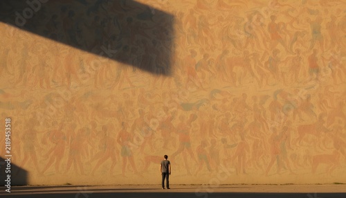 A small distant figure posing against a vast mural wall, warm afternoon light