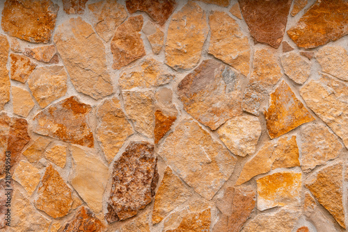Fotografie Natural stone wall texture with irregular shapes and warm earthy tones