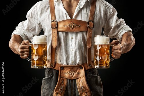 Man in Bavarian lederhosen holding two beer mugs isolated on black background with clipping path, Oktoberfest concept