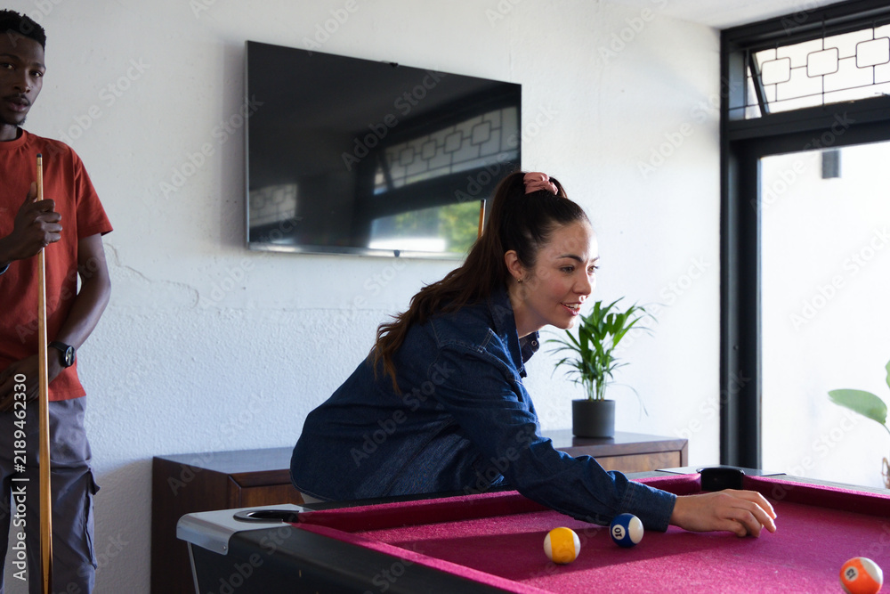 Fototapeta premium Diverse couple playing pool on burgundy-felt table in living room, female in denim jacket