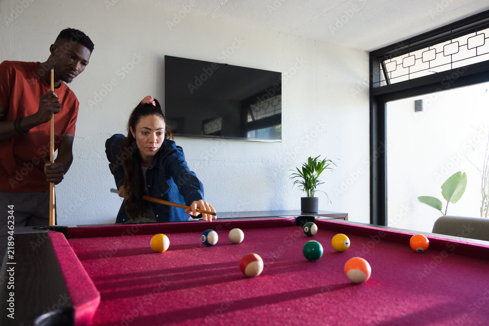 Obraz premium Diverse friends playing pool at home, woman lining up shot on magenta table, two cues, balls