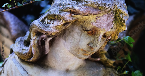 Close-up of a weathered mourning angel statue covered with moss and traces of decay, symbolic image of grief, mortality, remembrance and the passage of time.