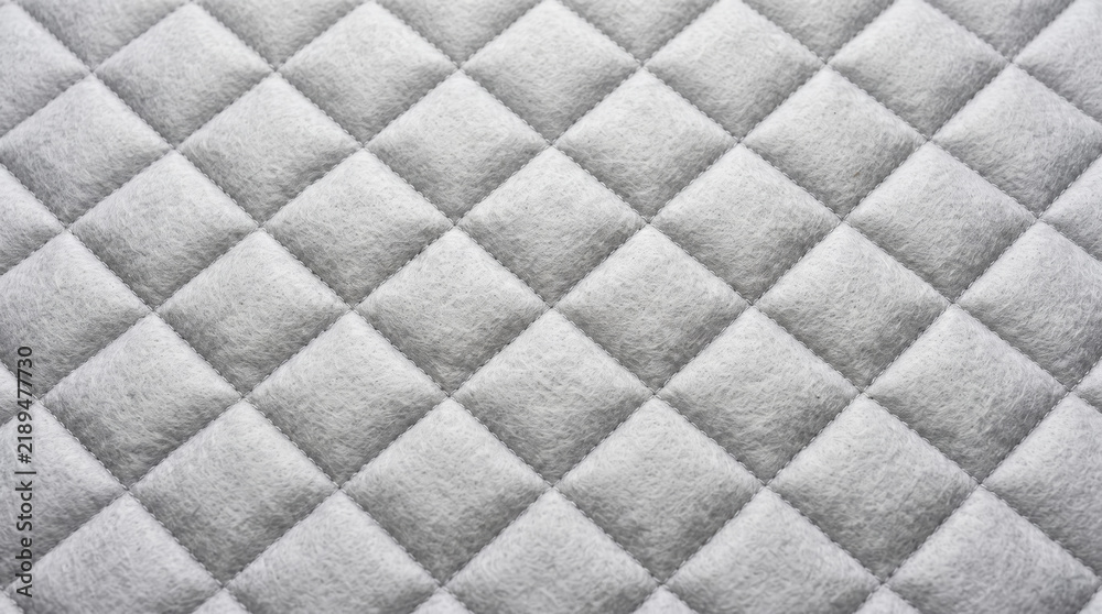 Obraz premium Quilted textile presenting a uniform gray diamond pattern with visible stitching, providing a soft textured background ideal for themes of comfort, warmth, and contemporary design
