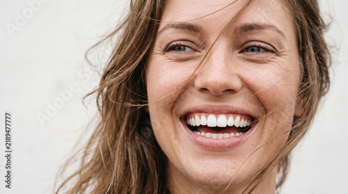 Close up of smiling young woman laughing with windblown hair, bright white teeth and genuine joy, conveying carefree wellbeing, optimism and authentic happiness