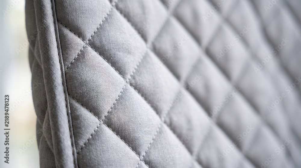 Fototapeta premium Quilted fabric texture creating a soft padded surface, forming a repetitive diamond pattern, useful for upholstery design, fashion material, and cozy textile backgrounds