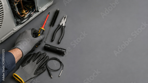 Heat pump maintenance technician using hand tool near open mechanical unit