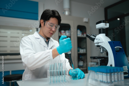 Young Asian scientist using pipette to fill test tubes with blue liquid in laboratory