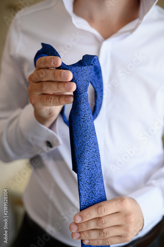 Cuadro en lienzo Man hands tying blue necktie close up, elegant groom wedding morning preparation