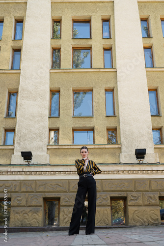Portrait of an attractive young caucasian woman wearing a yellow and black striped blouse near a building. Looking at camera. Fashion, style, beauty.