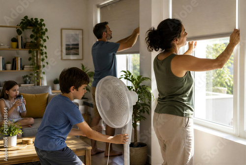 Family Closing Window Blinds and Turning On Fan During Heatwave at Home